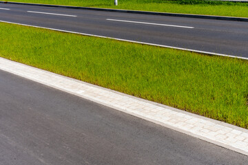 Modern asphalt road with green grass median strip on sunny day, illustrating urban infrastructure and landscaping
