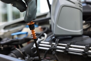 Worker checking motor oil level in car with dipstick, closeup