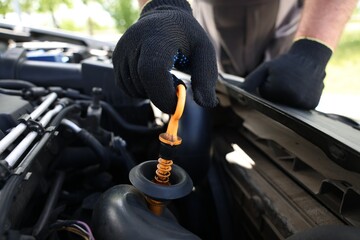 Worker checking motor oil level in car with dipstick, closeup