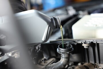 Pouring motor oil from bottle into car engine, closeup