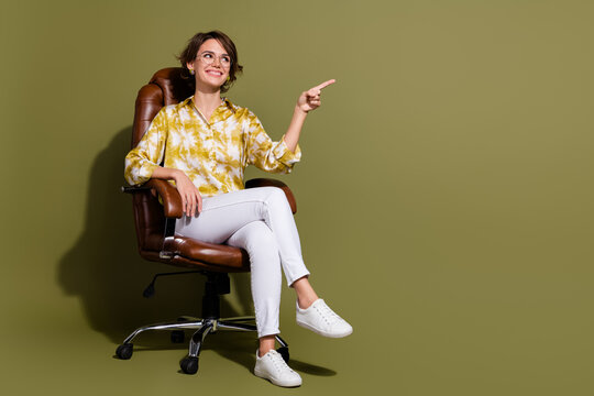 Fototapeta Young businesswoman in elegant blouse sits confidently in chair against khaki backdrop pointing forward