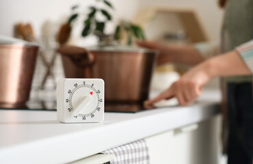 Kitchen timer against woman turning on stove in room, closeup
