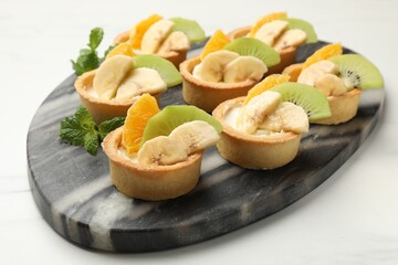 Tartlets with fruits and mint on white marble table, closeup. Delicious dessert