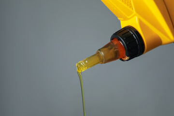Pouring motor oil from yellow canister on grey background, closeup. Space for text