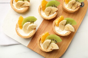Tartlets with fruits on white table, top view. Delicious dessert