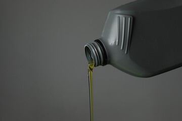 Pouring motor oil from canister on grey background, closeup. Space for text