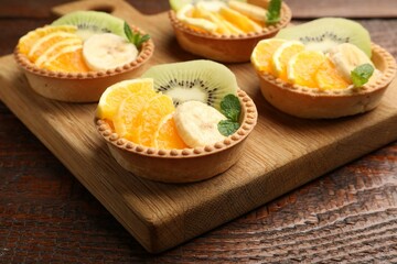 Tartlets with fruits and mint on wooden table, closeup. Delicious dessert