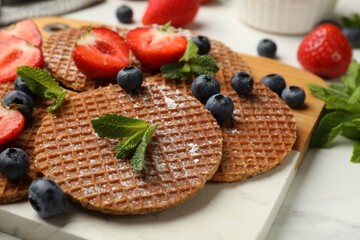 Tasty Dutch waffles (stroopwafels), mint and strawberries on white marble table, closeup