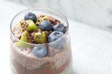 Delicious chocolate pudding with chia seeds, kiwi and blueberries in glass on blurred light background, closeup. Space for text