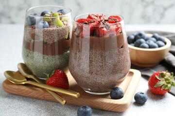 Delicious chocolate puddings with chia seeds and berries in glasses on grey textured table against...