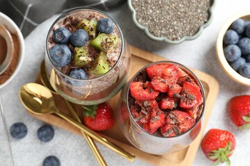 Delicious chocolate puddings with chia seeds and berries in glasses on grey table, flat lay