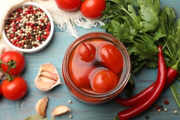 Tasty pickled tomatoes in jar and ingredients on light blue wooden table, flat lay
