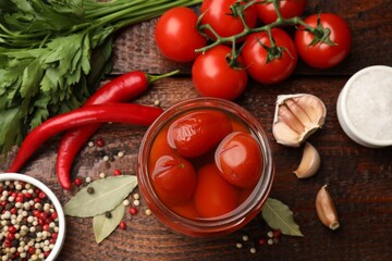 Tasty pickled tomatoes in jar and ingredients on wooden table, flat lay