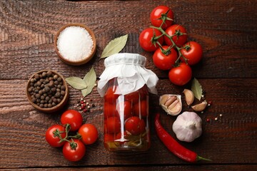 Tasty pickled tomatoes in jar and ingredients on wooden table, flat lay