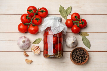 Tasty pickled tomatoes in jar and ingredients on wooden table, flat lay