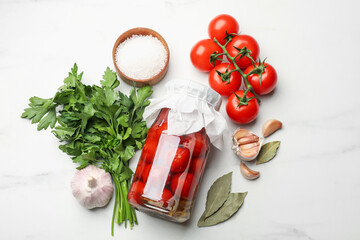Tasty pickled tomatoes in jar and ingredients on white marble table, flat lay