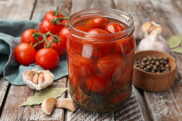 Tasty pickled tomatoes in jar and ingredients on wooden table, closeup