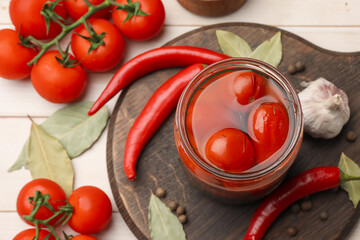 Tasty pickled tomatoes in jar and ingredients on wooden table, flat lay