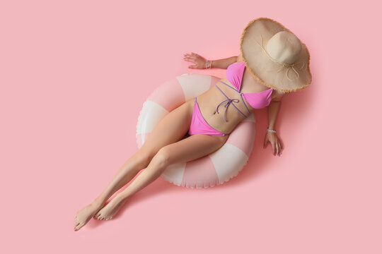Young woman in swimsuit with swim ring lying on pink background, top view