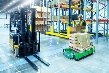Man working in warehouse. Autonomous robot moves pallets. Forklift near storekeeper. Man standing in modern warehouse. Manager of enterprise storage area. Warehouse with unmanned forklift