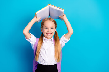 Young schoolgirl holding an open book above her head, smiling joyfully, on a bright blue...