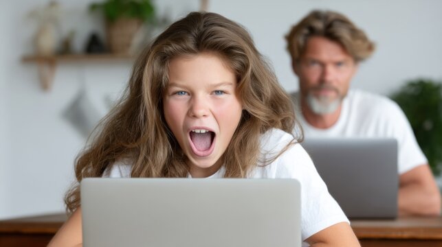 child shows clear frustration while staring at a laptop screen, with an adult sitting behind, also working on another laptop in a well-lit home office