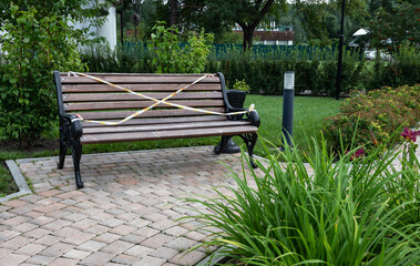 Park bench with caution tape in a garden setting.