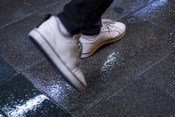 A close-up shot of a person's foot in a white sneaker stepping on a wet pavement. This image captures the essence of urban life and movement.