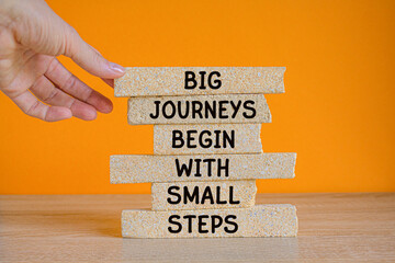 Brick blocks with words BIG JOURNEYS BEGIN WITH SMALL STEPS. Businessman hand. Beautiful orange...