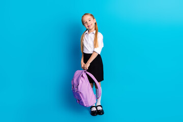 Confident young schoolgirl in uniform holding purple backpack smiling against vivid blue background