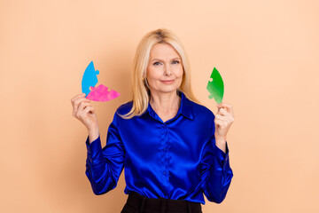 Elegant senior businesswoman holding colorful puzzle pieces against a beige background, symbolizing challenges and teamwork