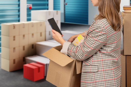 Woman near storage unit. Girl with boxes on warehouse territory. Cropped lady with phone at pantries doors. Woman brought boxes to storage unit. Warehouse rent concept. Self storage unit