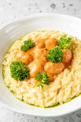 Creamy risotto with orange sauce and parsley garnish in a white bowl on stone background, top view. Ideal for food photography, restaurant menus, or culinary blogs