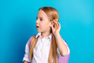 Young schoolgirl with long blonde hair wearing a school uniform listening closely with a curious...