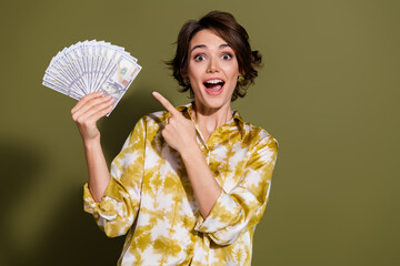 Excited young businesswoman with cheerful expression holding cash against khaki background,...