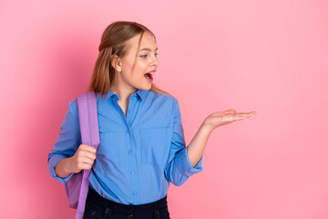 Young schoolgirl gesturing with open hand against pink backdrop holding backpack, showcasing a...