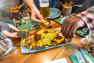 Friends sharing nachos with guacamole, cheese and jalapenos at restaurant table
