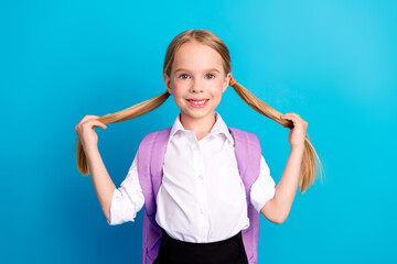 Smiling schoolgirl in uniform with ponytails holding her pigtails against a solid blue background