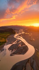 Fototapeta premium Aerial shot of a winding river at sunset, surrounded by dramatic landscapes and vibrant skies.
