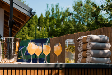 Luxurious Outdoor Summer Party Scene with Cocktails, Towels, and Bar Setup on a Sunny Patio with Wooden Fence.