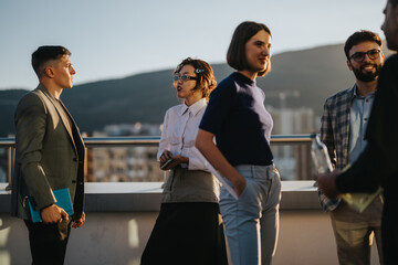 Diverse colleagues engage in a brainstorming session on a high-rise balcony at sunset. They are...