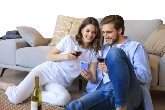 Happy couple sitting, relaxing on floor in living room, drinking red wine. Smiling young husband and wife rest at home enjoy romantic date on family weekend together on a transparent background