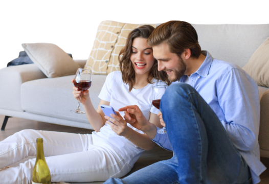 Happy couple sitting, relaxing on floor in living room, drinking red wine. Smiling young husband and wife rest at home enjoy romantic date on family weekend together on a transparent background
