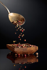 Black, red, white, and allspice peppercorns is poured in wooden dish.