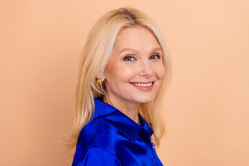 Confident mature businesswoman wearing a stylish blue shirt, smiling warmly against a soft beige...