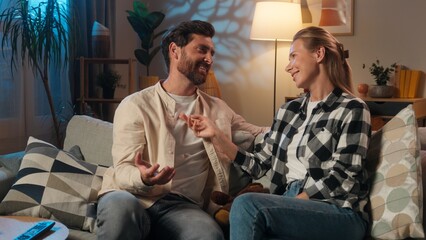Caucasian joyful man with woman couple married female male talking relaxed on sofa in living room...