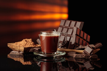 Mug of hot chocolate against broken bitter chocolate bars and dish with cocoa powder.