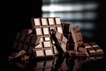 Broken bitter chocolate bars on a black glossy background.