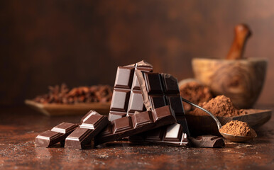 Broken dark chocolate bar and cocoa powder on a brown table.