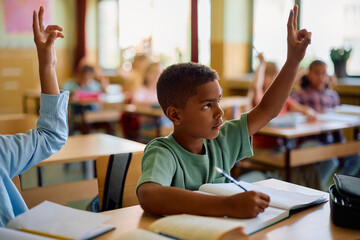 Black schoolboy raising hand to answer question in classroom.